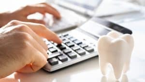 A close-up shot of hands using a calculator next to a model of a tooth.