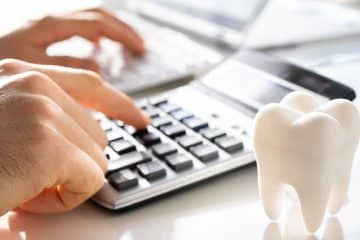A close-up shot of hands using a calculator next to a model of a tooth.