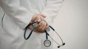 A person wearing a white lab coat holds a stethoscope behind their back.